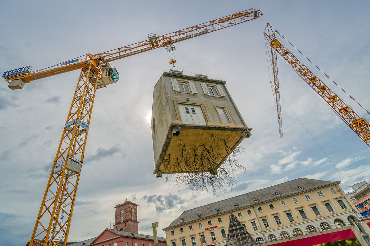 Karlsruhe feiert den 300. Stadtgeburtstag. Das zentrale Kunstwerk der Ausstellung »Die Stadt ist der Star« stellt die Installation »Pulled by the Roots« des argentinischen Künstlers Leandro Erlich dar. Am Marktplatz in Karlsruhe steht ein großer Baukran, der eine ungewöhnliche Last trägt: An seinen Stahlseilen hängt ein ganzes Haus!